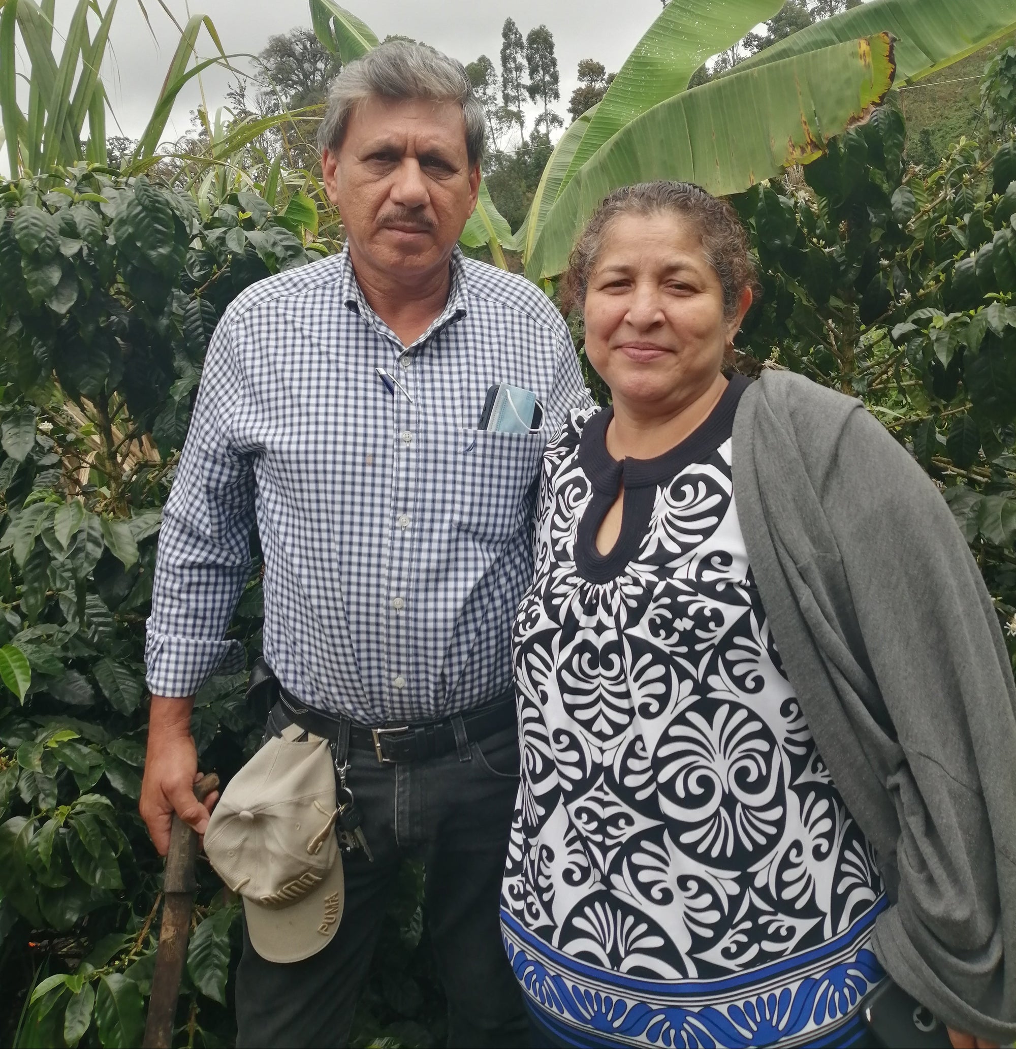 Husband-and-wife coffee growers Roger and Isabel on their farm, Las Mercedes. Roger wears a blue checked shirt and Isabel wears a grey cardigan over a black and white patterned top.